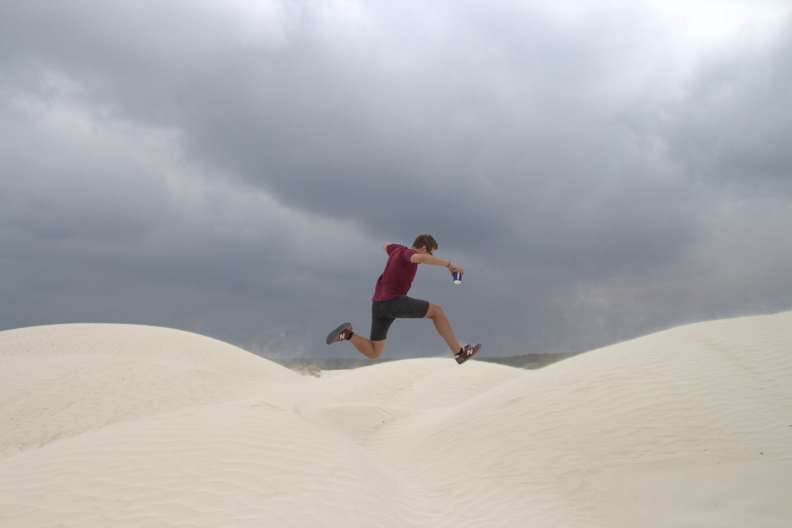 Jumping on white sand dunes with a coffee in hand